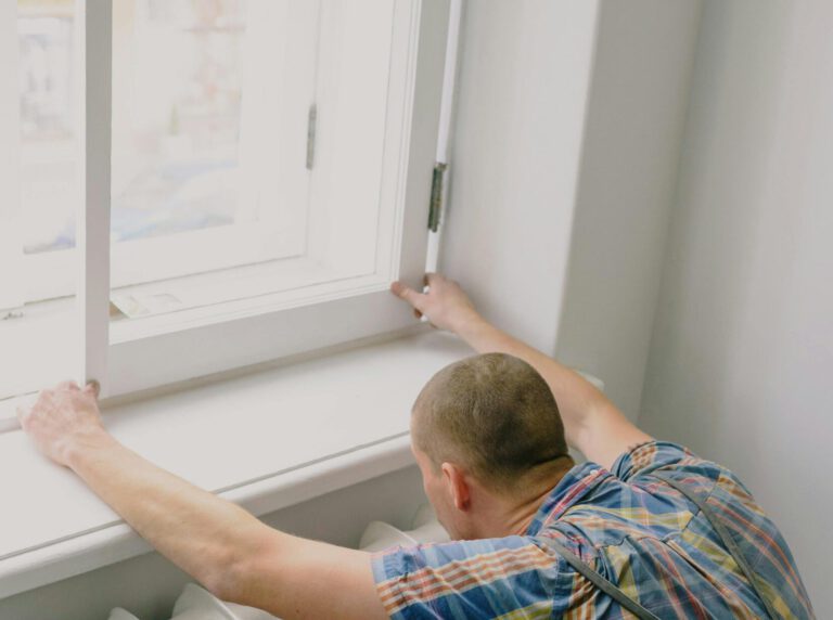 Back view of unrecognizable fitter in dirty apron installing window above radiator while doing home renovation